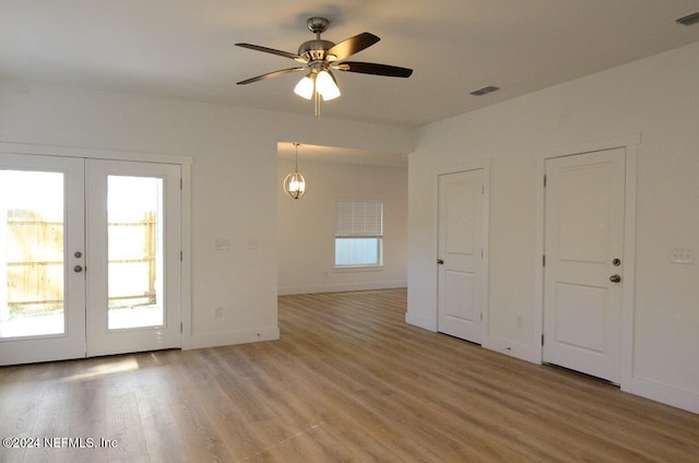 spare room with french doors, light hardwood / wood-style floors, and ceiling fan with notable chandelier