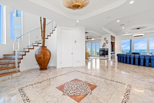 foyer featuring a tray ceiling, ceiling fan, plenty of natural light, and a multi sided fireplace