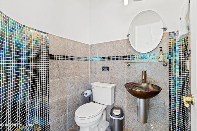 bathroom featuring toilet, tile walls, and sink