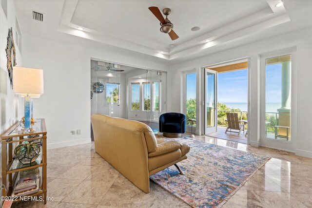 living room with a tray ceiling, ceiling fan, and a healthy amount of sunlight