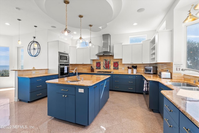 kitchen featuring pendant lighting, a kitchen island with sink, white cabinets, wall chimney exhaust hood, and stainless steel appliances