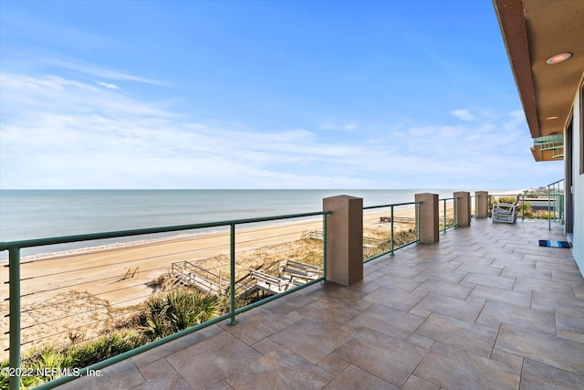 view of patio / terrace featuring a water view, a balcony, and a view of the beach