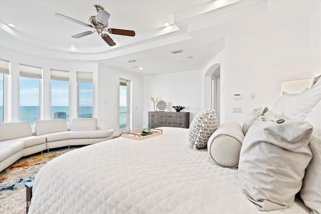 bedroom featuring a tray ceiling, ceiling fan, and a water view