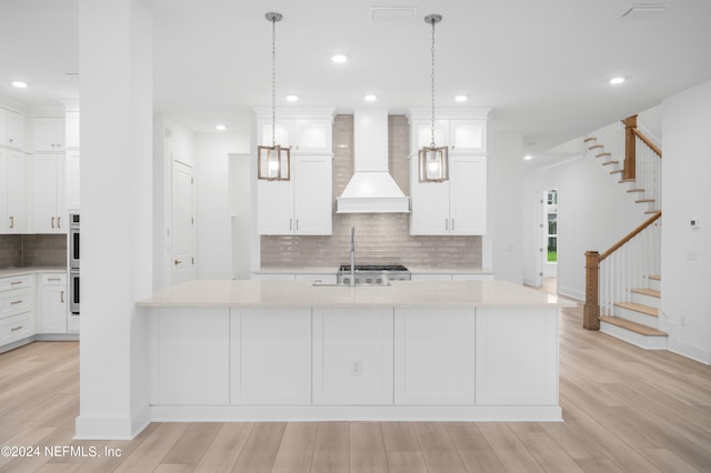 kitchen featuring light hardwood / wood-style floors, an island with sink, custom exhaust hood, and light stone countertops