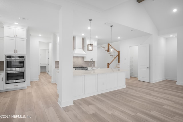 kitchen with stainless steel double oven, white cabinets, custom range hood, decorative backsplash, and pendant lighting