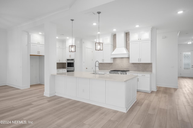 kitchen with custom range hood, hanging light fixtures, a kitchen island with sink, white cabinets, and a sink