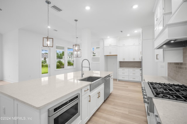 kitchen with visible vents, hanging light fixtures, appliances with stainless steel finishes, an island with sink, and custom range hood