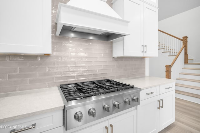 kitchen with premium range hood, white cabinetry, light wood-type flooring, decorative backsplash, and stainless steel gas stovetop