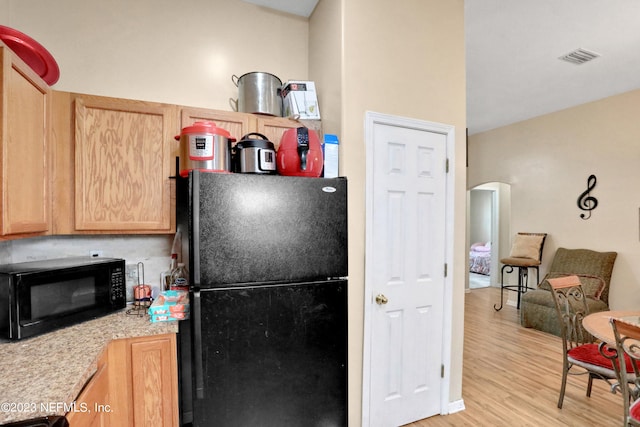 kitchen with light brown cabinetry, light wood-type flooring, and black appliances