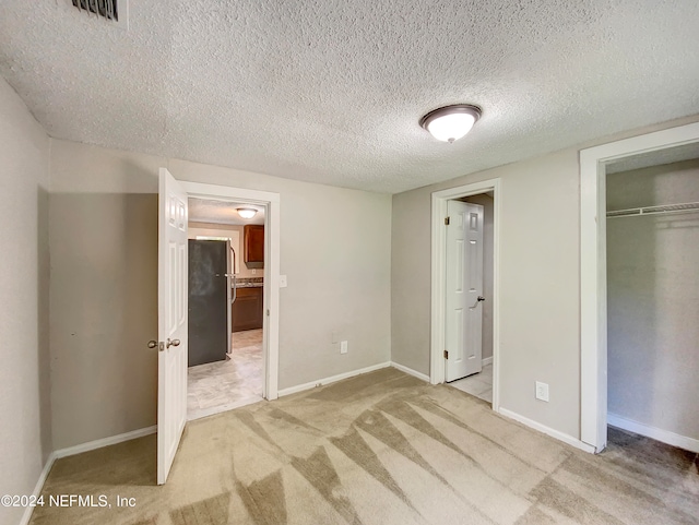 unfurnished bedroom with a textured ceiling, refrigerator, light colored carpet, and a closet