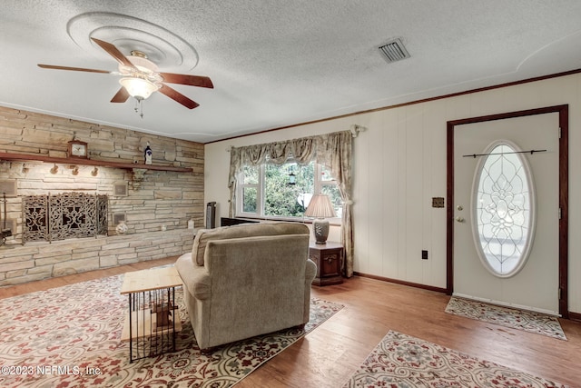 living room featuring ceiling fan, a fireplace, light hardwood / wood-style floors, and a textured ceiling