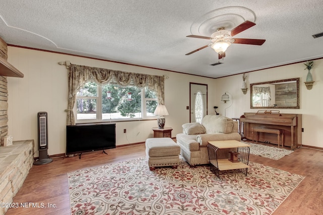 living room with ceiling fan, ornamental molding, a textured ceiling, and light wood-type flooring