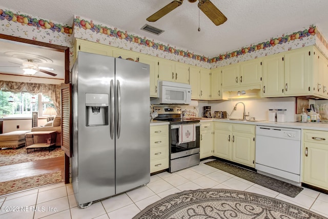 kitchen with appliances with stainless steel finishes, sink, light tile patterned floors, ceiling fan, and a textured ceiling