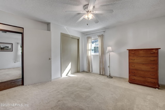 unfurnished bedroom with ceiling fan, light carpet, a textured ceiling, and a closet