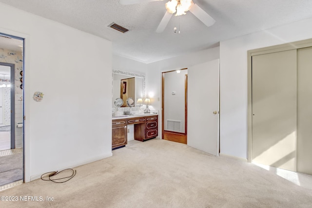 bedroom featuring ceiling fan, light colored carpet, ensuite bathroom, and a textured ceiling