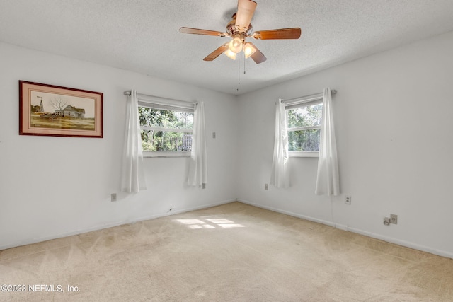 empty room with ceiling fan, light colored carpet, and a textured ceiling