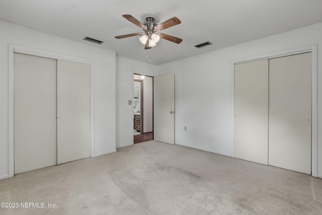 unfurnished bedroom with ceiling fan, light colored carpet, and two closets