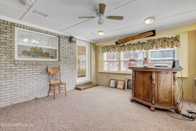 interior space featuring ceiling fan, carpet, a healthy amount of sunlight, and brick wall