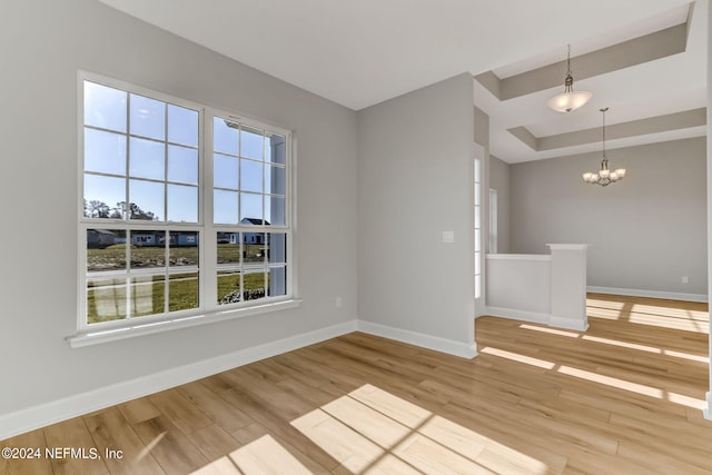 empty room with a tray ceiling, light wood-type flooring, and an inviting chandelier