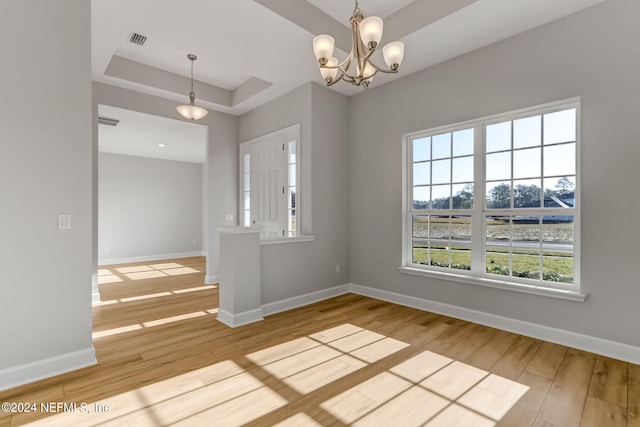 unfurnished room featuring a tray ceiling, light wood-type flooring, and a notable chandelier