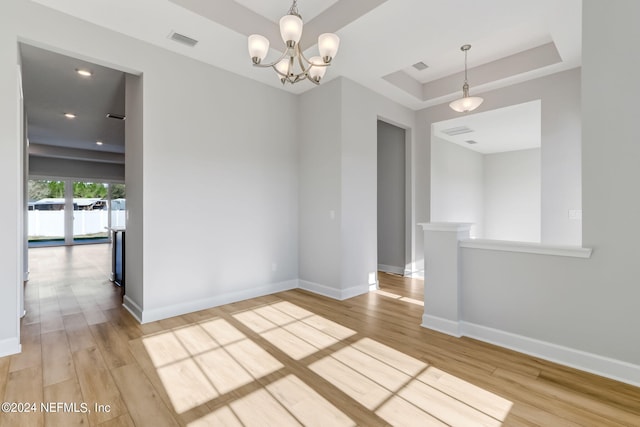 spare room with a notable chandelier, light hardwood / wood-style floors, and a tray ceiling