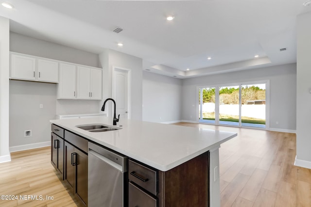 kitchen featuring stainless steel dishwasher, a raised ceiling, a kitchen island with sink, sink, and white cabinets