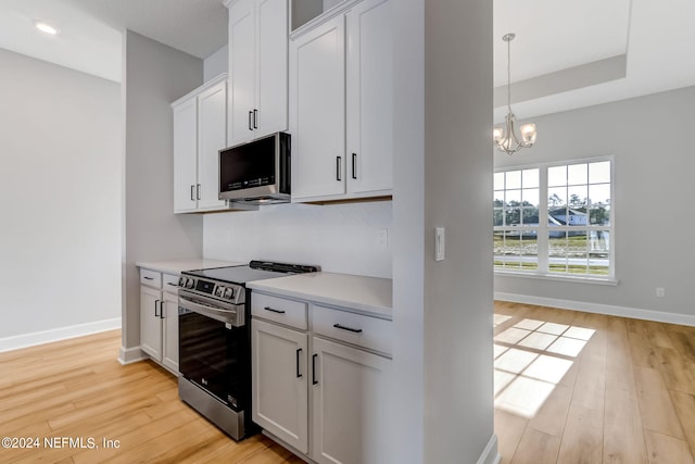 kitchen with white cabinetry, pendant lighting, a chandelier, appliances with stainless steel finishes, and light wood-type flooring