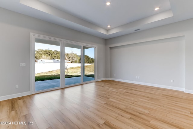 empty room featuring a raised ceiling and light hardwood / wood-style flooring