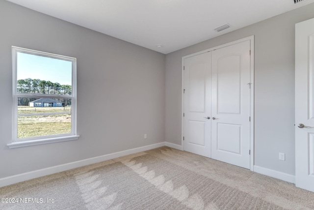 unfurnished bedroom featuring multiple windows, light carpet, and a closet