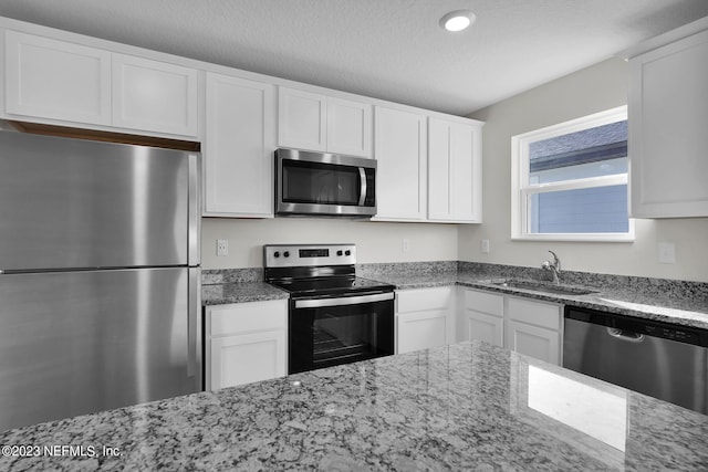 kitchen featuring stainless steel appliances, a textured ceiling, light stone countertops, and white cabinetry