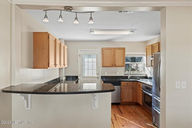 kitchen with light wood-type flooring, kitchen peninsula, appliances with stainless steel finishes, and hanging light fixtures