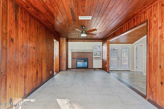 unfurnished living room featuring ceiling fan, a brick fireplace, french doors, wooden walls, and wooden ceiling