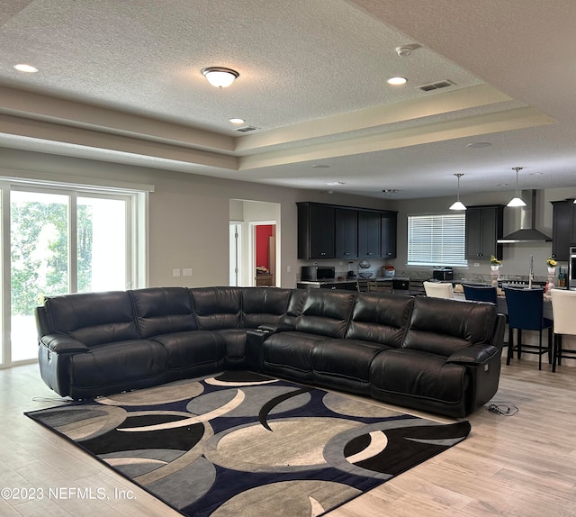 living room with a textured ceiling, a raised ceiling, and light hardwood / wood-style floors