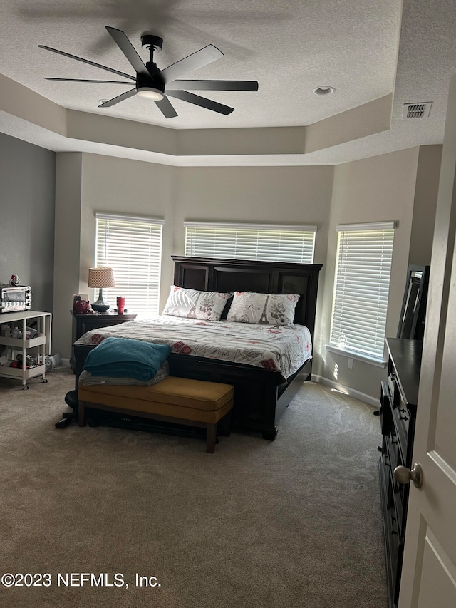 carpeted bedroom featuring a textured ceiling, ceiling fan, and a raised ceiling