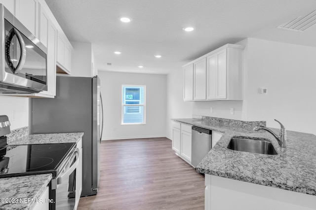 kitchen featuring visible vents, white cabinets, stainless steel appliances, light wood-type flooring, and a sink