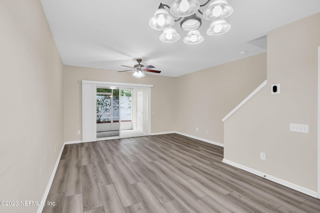 empty room featuring ceiling fan with notable chandelier and light hardwood / wood-style floors