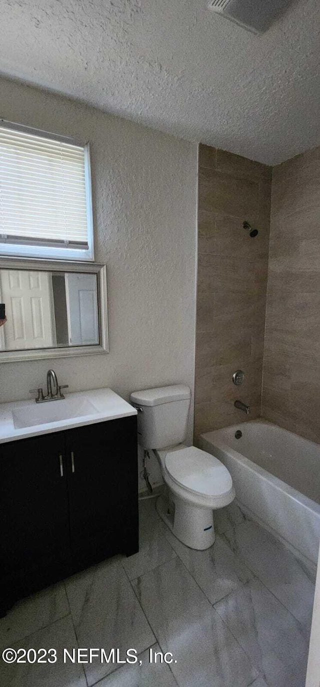 full bathroom featuring a textured ceiling, tiled shower / bath combo, vanity, and toilet