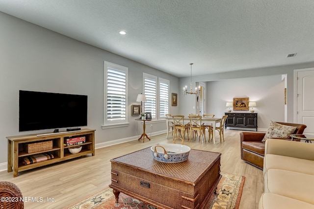 living room with a notable chandelier, a textured ceiling, and light hardwood / wood-style flooring