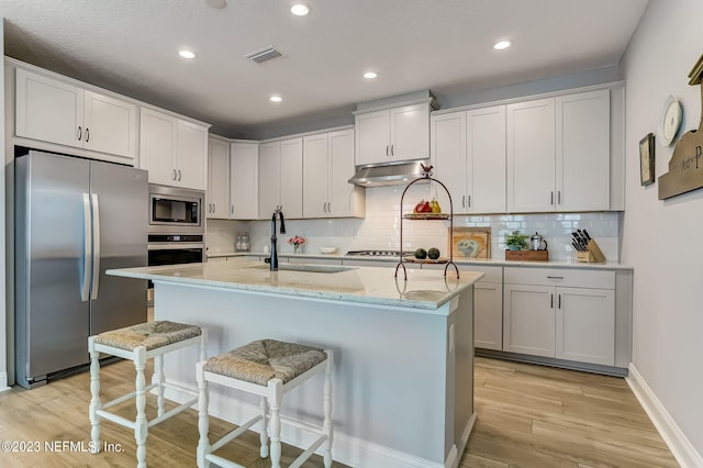 kitchen with a breakfast bar, a kitchen island with sink, white cabinets, light hardwood / wood-style floors, and stainless steel appliances