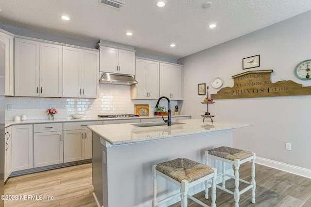 kitchen featuring a kitchen bar, light stone counters, sink, and a center island with sink