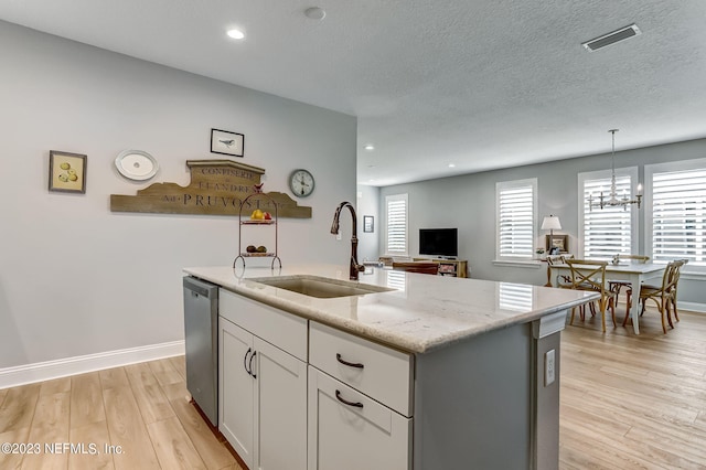 kitchen with dishwasher, sink, hanging light fixtures, light stone countertops, and an island with sink