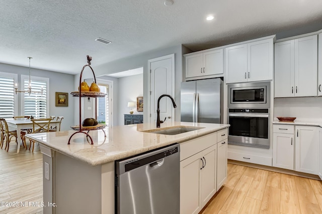 kitchen with white cabinets, stainless steel appliances, a kitchen island with sink, and sink