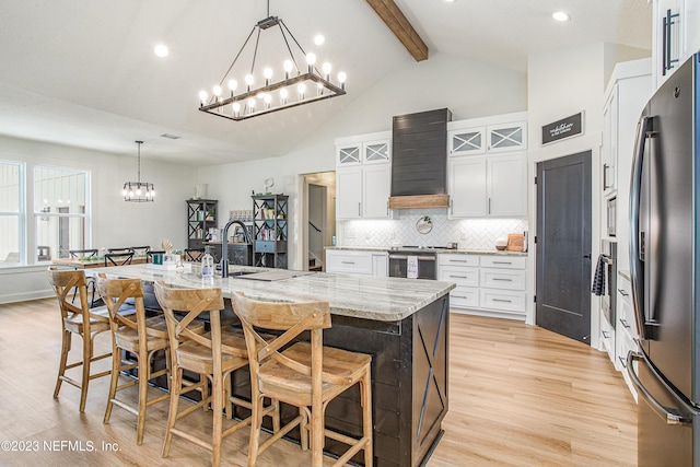 kitchen featuring light stone countertops, stainless steel appliances, a kitchen island with sink, white cabinets, and custom exhaust hood