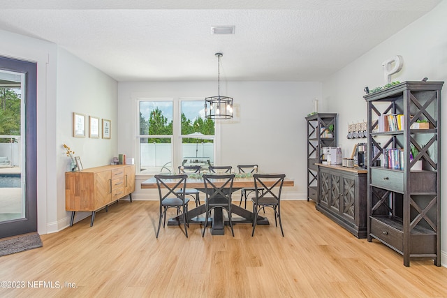 dining area featuring a textured ceiling, a notable chandelier, and light wood-type flooring