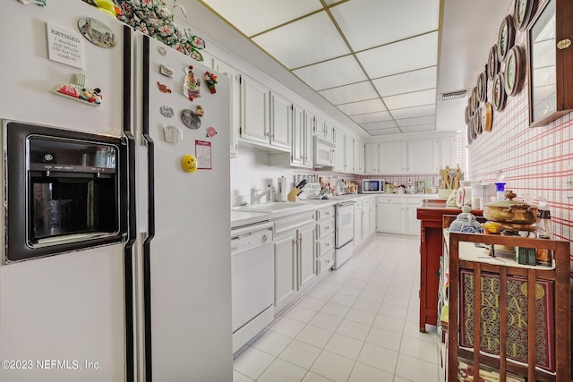 kitchen with a drop ceiling, white appliances, sink, light tile patterned floors, and white cabinetry