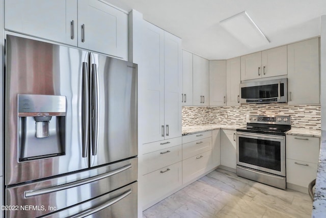 kitchen featuring stainless steel appliances, light stone countertops, white cabinets, and backsplash