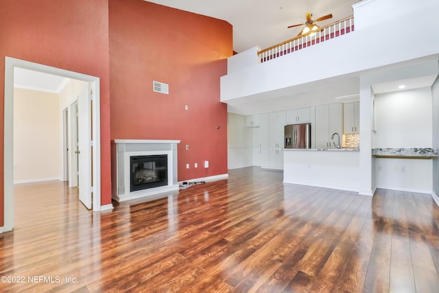 unfurnished living room featuring wood-type flooring, ceiling fan, and a high ceiling