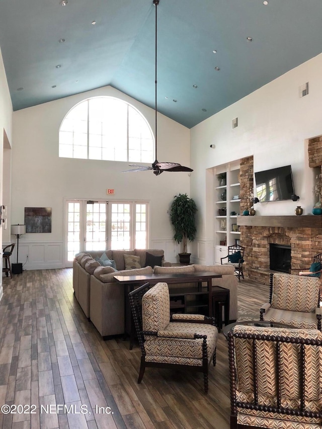 living room with built in shelves, a stone fireplace, dark hardwood / wood-style floors, ceiling fan, and a high ceiling