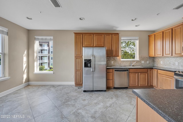 kitchen with stainless steel appliances, backsplash, dark stone countertops, sink, and light tile floors