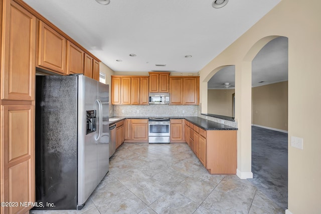 kitchen featuring arched walkways, a ceiling fan, appliances with stainless steel finishes, tasteful backsplash, and dark countertops